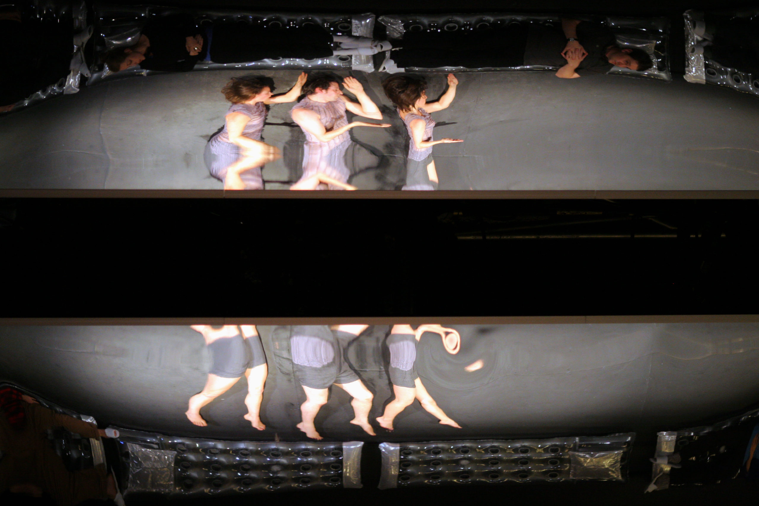 Distorted reflection of three dancers lying on their left side with a large black stripe in the middle of the photo
